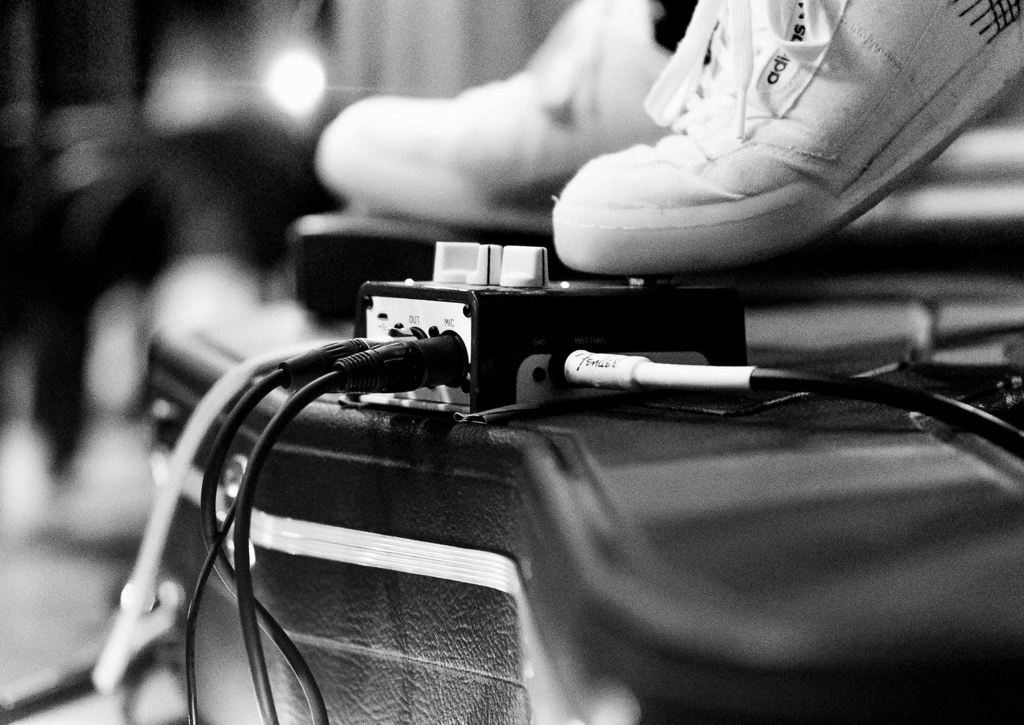 Black and white close-up of a guitar pedalboard and cabling on top of a PA cabinet