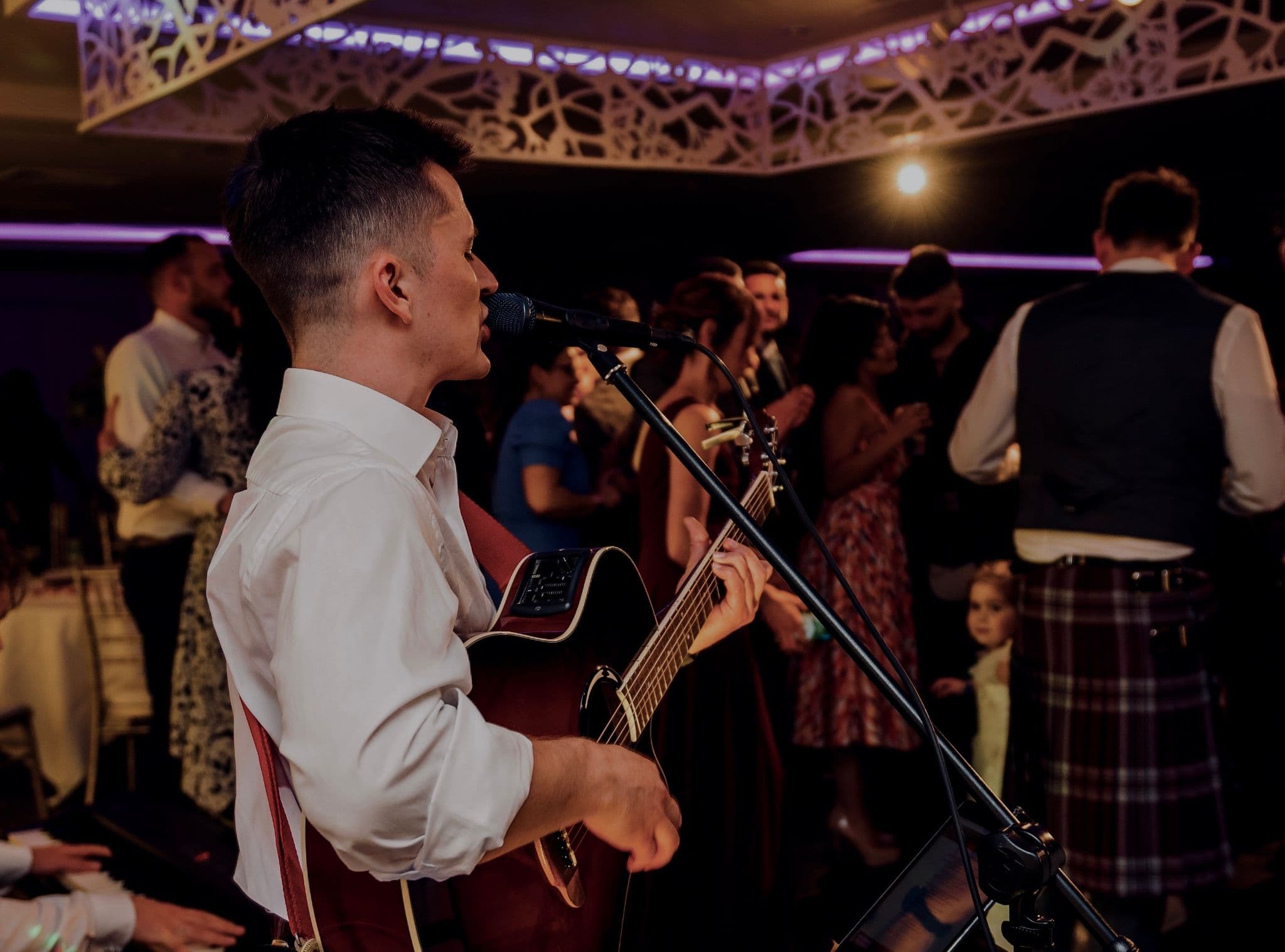 Robbie Wisniewski performing to kilted guests dancing in an uplit function room