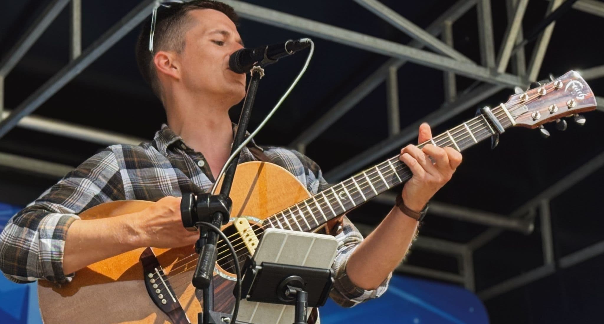 Robbie Wisniewski singing and playing acoustic guitar under a marquee at an evening event